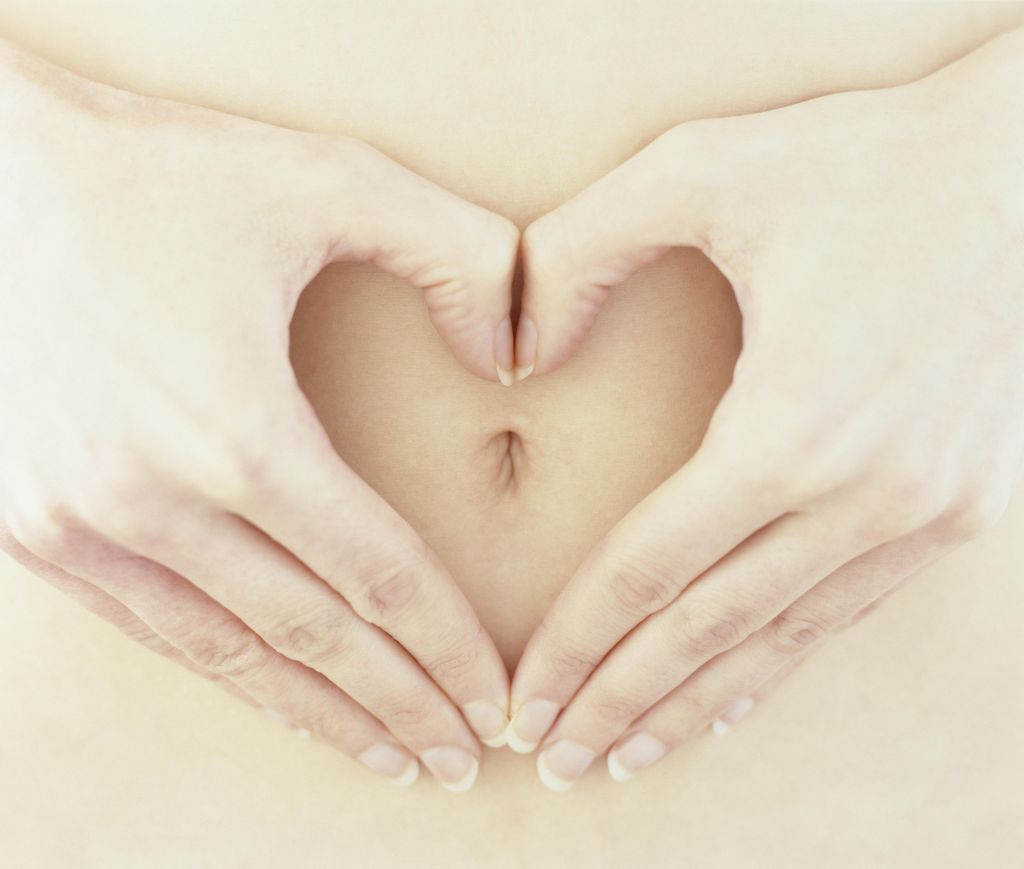 Woman making heart shape with hands around belly button, close-up