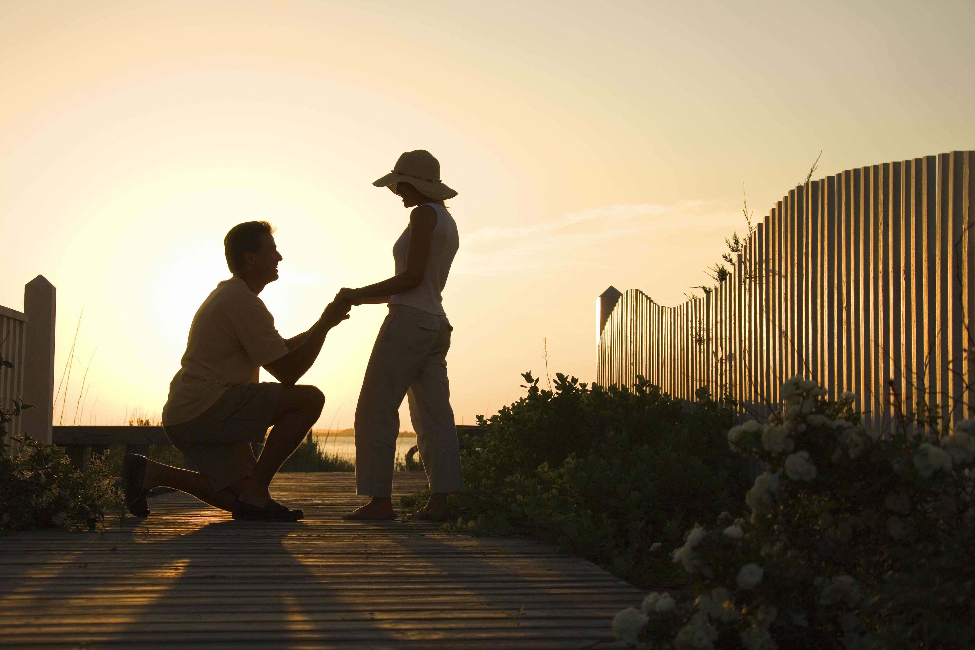 Silhouette of man proposing to woman on beach boardwalk