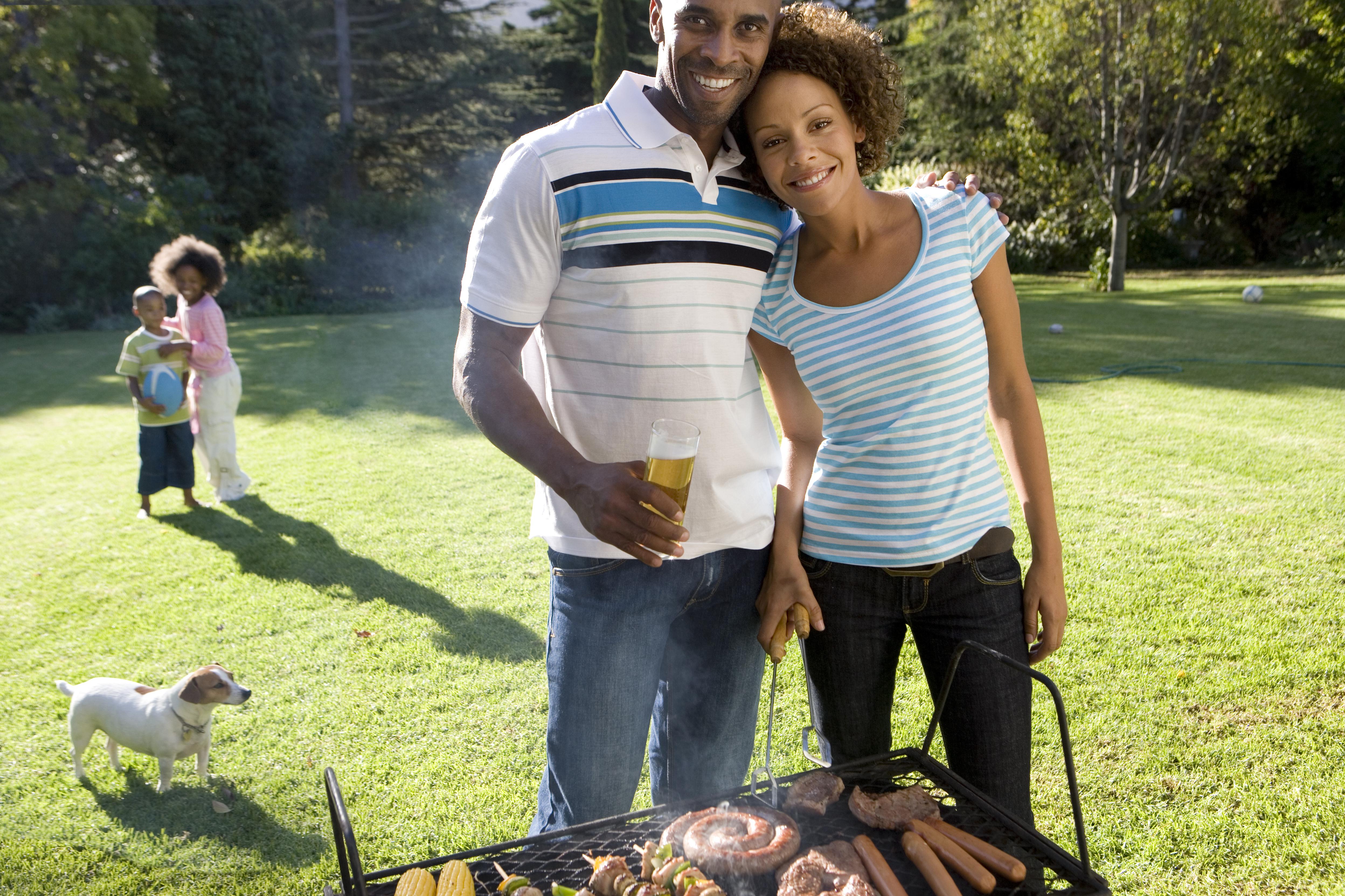 Couple by barbeque, son and daughter (6-10) in background, smiling, portrait