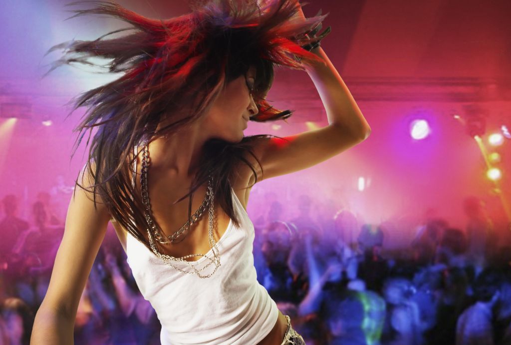 Young female DJ at record decks in nightclub, arm raised