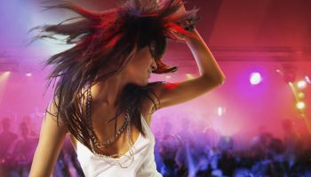 Young female DJ at record decks in nightclub, arm raised