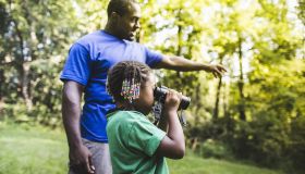 Father and daughter watching with binoculars in forest eco camp