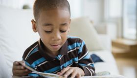 African American boy reading book on sofa