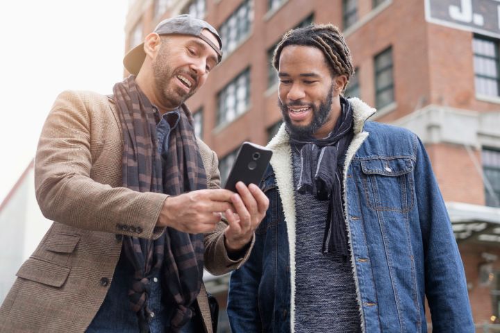 Smiley homosexual couple taking selfie with smart phone in street