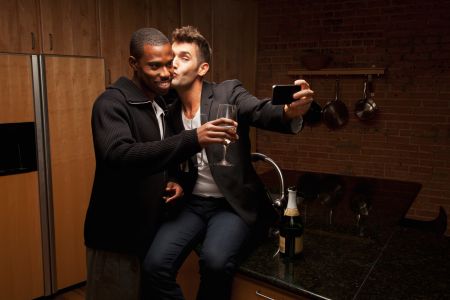Gay couple drinking wine in kitchen and taking self-portraits