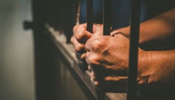 Cropped Hands Of Male Prisoner Holding Prison Bars