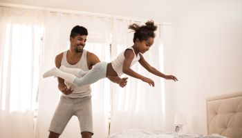 Playful black father and daughter having fun in bedroom in the morning.