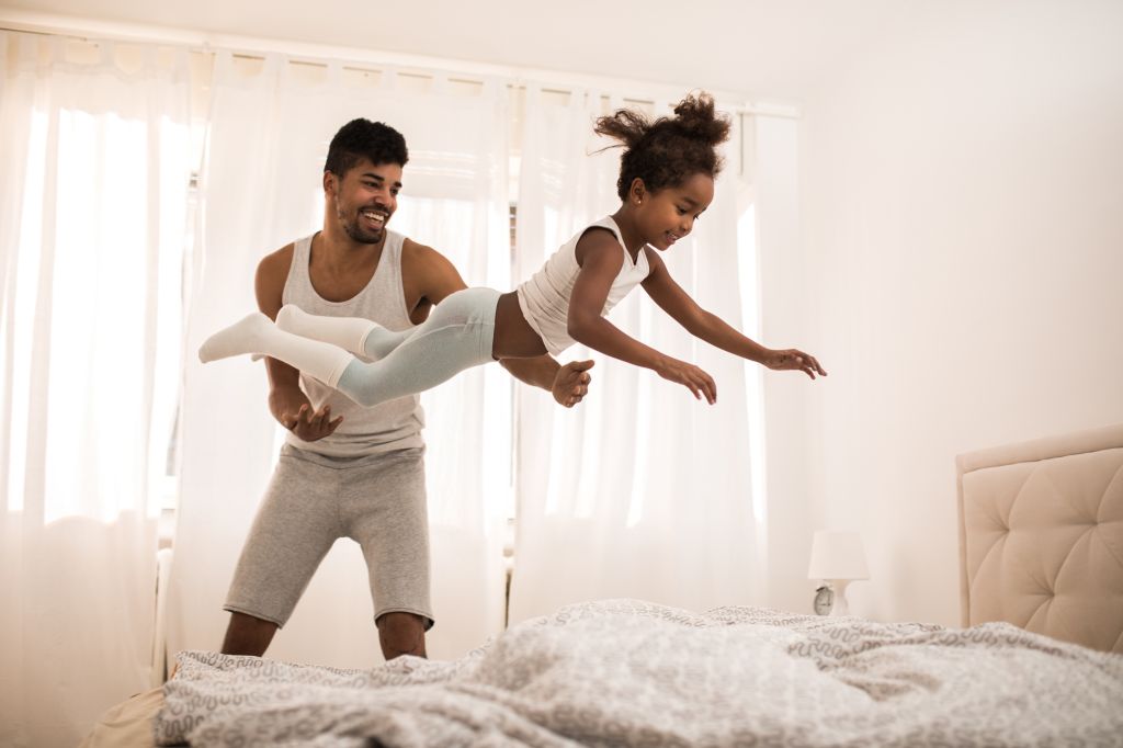 Playful black father and daughter having fun in bedroom in the morning.