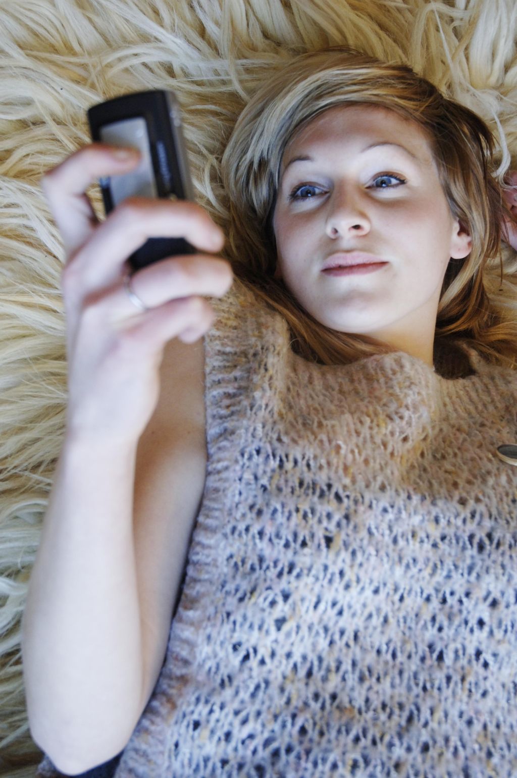 A young woman, lying on the floor, texting on a mobile phone.