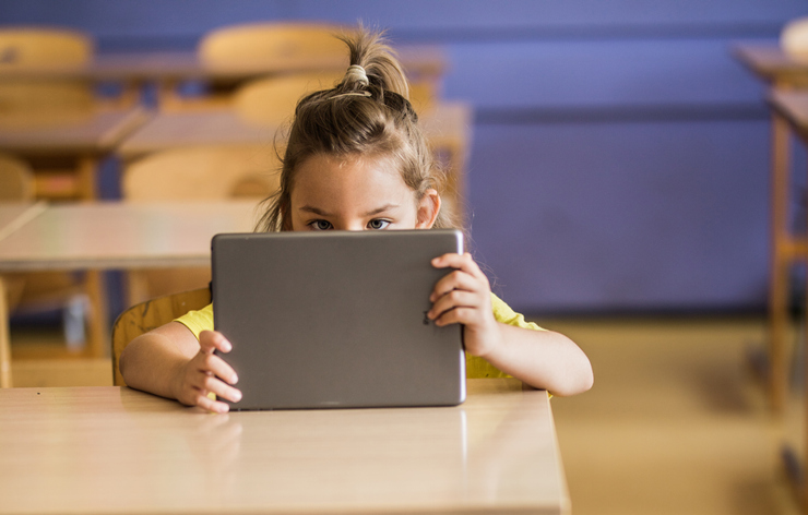 Cute schoolgirl using digital tablet on a class at elementary school.