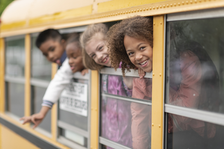 Diverse group of students look out school bus windows