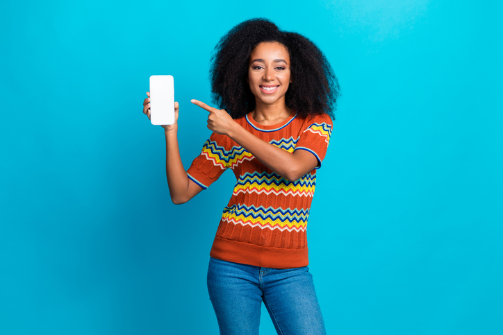 Photo of young girl promoting new updated software for mobile phone demonstrate pointing quality display isolated on blue color background