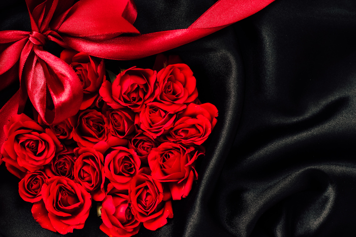 Red roses arranged with a satin ribbon on black fabric create a romantic atmosphere