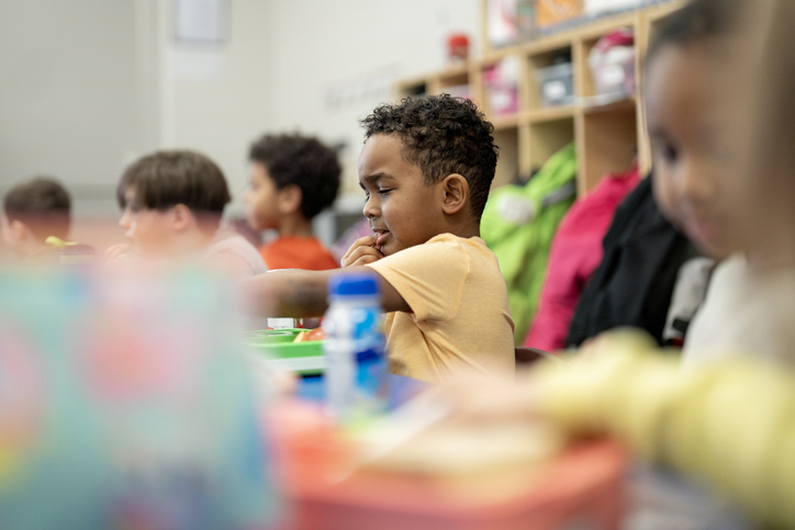 Young Children Eating Lunch in a Diverse Elementary Classroom With Backpacks and Lunchboxes
