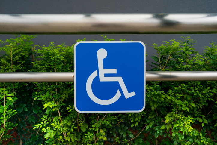 International Symbol of Access Blue Handicap Sign Mounted on Metal Railing with Green Foliage
