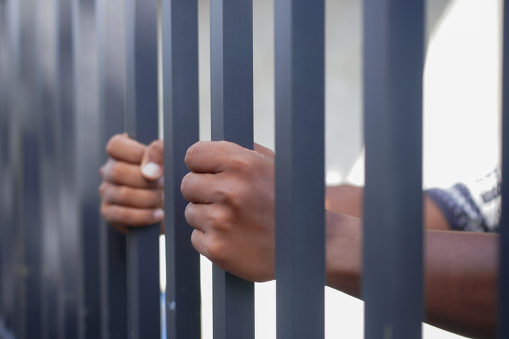 Close-up of hands gripping metal prison bars, symbolizing imprisonment, justice, crime, human rights, freedom restriction, and social issues. Concept of detention, punishment, and captivity.