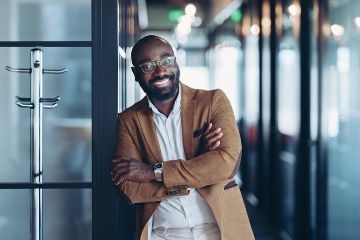 Smiling young man in business casual wear standing with crossed arms looking at the camera