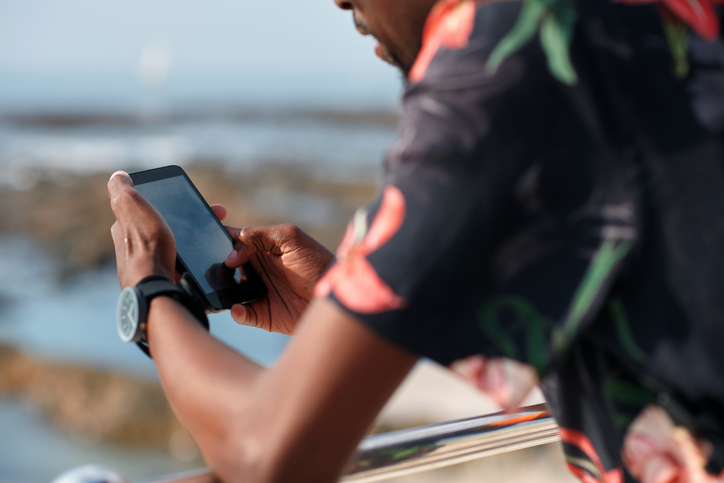 Phone, hands and man by beach on holiday for texting, social media or contact on mobile app. Technology, promenade and male person on cellphone for blog on vacation tips by ocean on weekend trip.