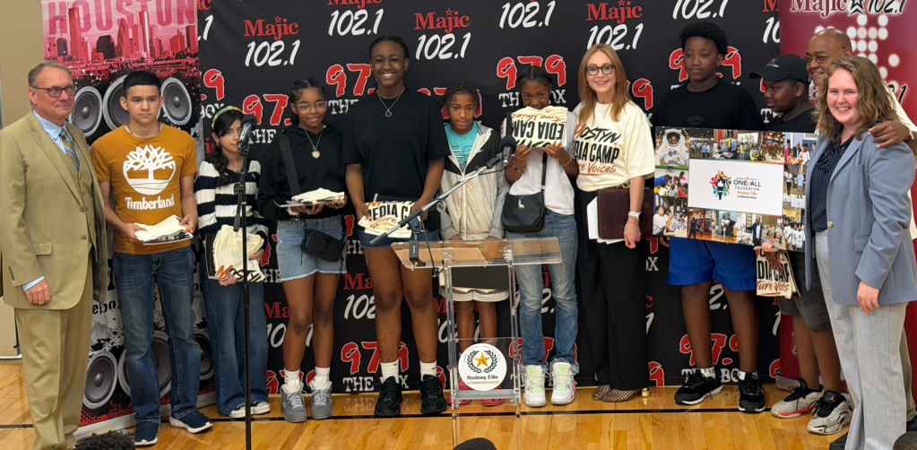 A group of young people standing in front of radio station branding for Magic 102.1, including a display with the station's logo and frequency.