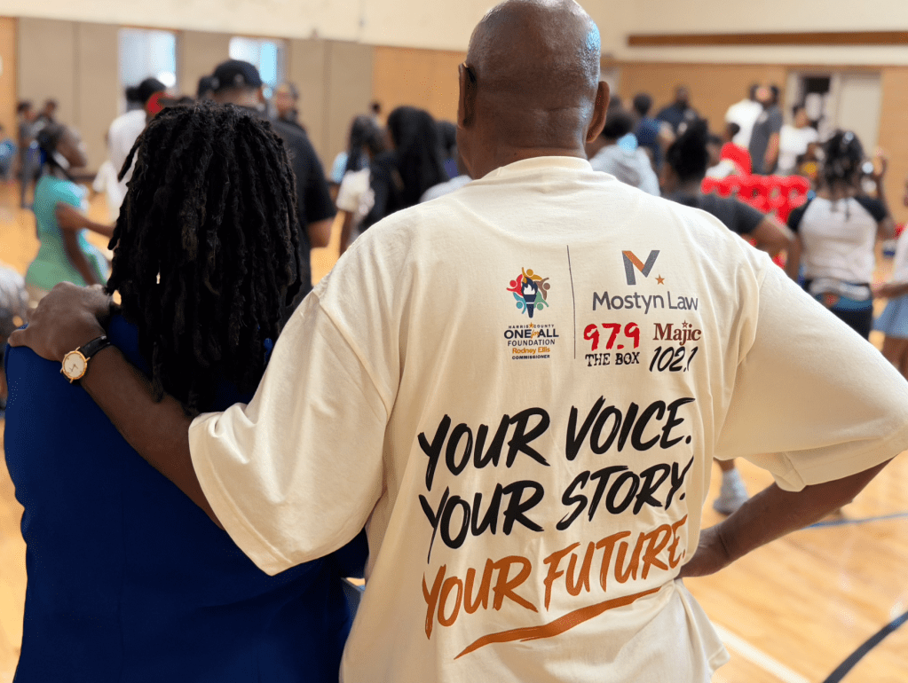 A crowd of people in a room, with a person wearing a white t-shirt that says "Your Voice. Your Story. Your Future.