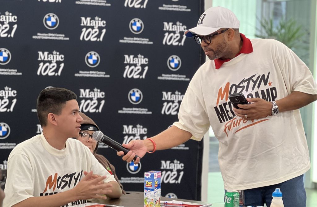 Two people wearing "Mostly Media" shirts, one being interviewed by the other in front of a Majic 102.1 radio station backdrop.