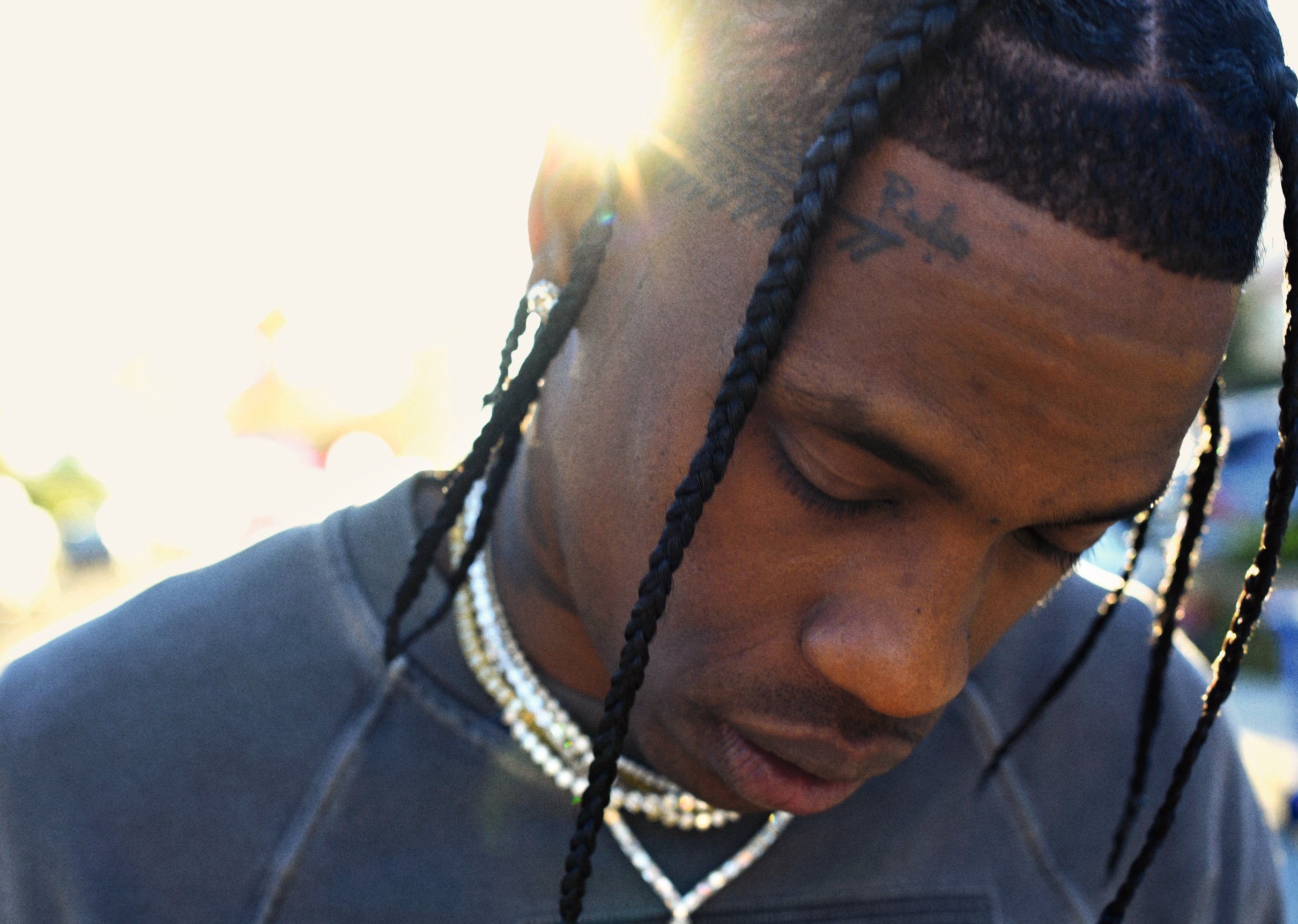 A close-up portrait of a young Black man with braided hair and facial tattoos, with a pensive expression on his face.