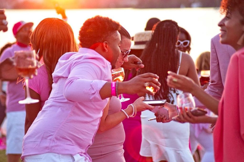 A group of people socializing and dancing at an outdoor party or event, holding drinks and enjoying themselves.