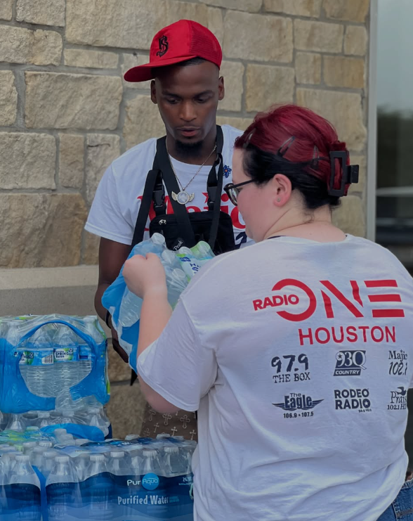 Two people in Radio One Houston branded apparel standing next to cases of bottled water.