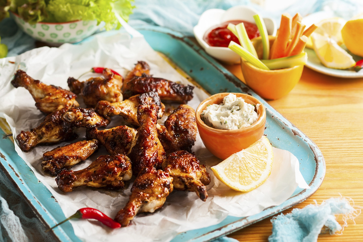 Delicious barbecue chicken wings with two sauces and carrot with celery on vintage serving tray