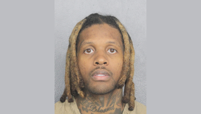 A close-up portrait of a man with dreadlocks and facial tattoos looking directly at the camera.