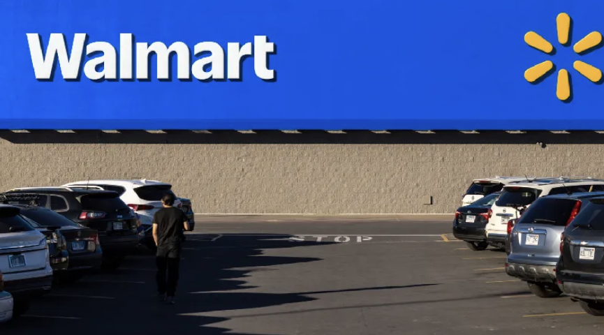 Walmart store exterior with large blue and yellow logo sign, parking lot with several vehicles.