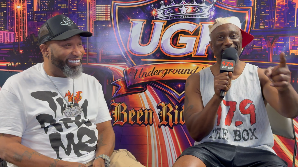 Two men, one wearing a "The Box" shirt and the other a "Def Jam" shirt, sitting on a set with a "UGI Underground" backdrop and logo.