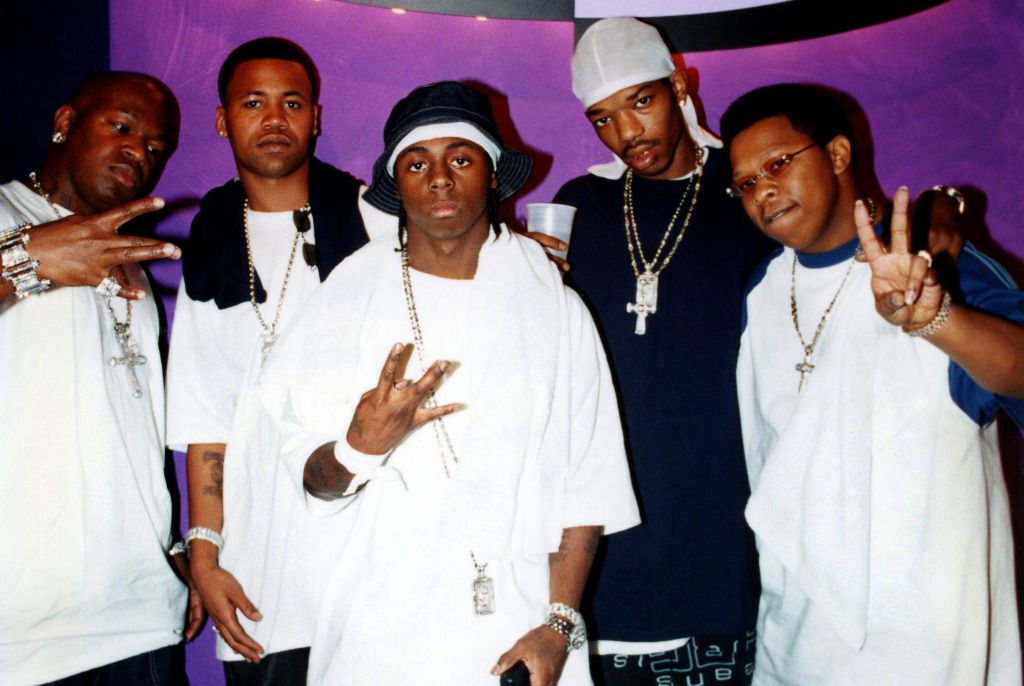 A group of rappers posing together in front of a "Jenny Jones" backdrop, including Birdman, Juvenile, Lil Wayne, B.G., and Mannie Fresh.