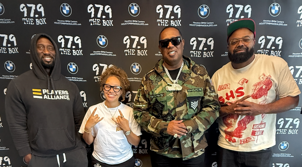 Four people posing in front of a backdrop with "97.9 THE BOX" and BMW logos.