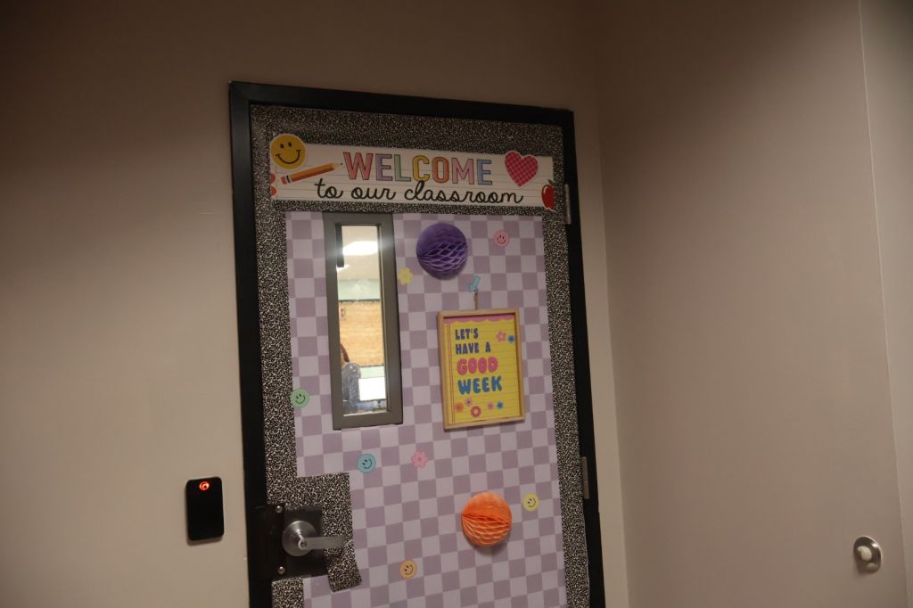 A classroom door with a "Welcome to our classroom" sign, featuring colorful decorations and a "Let's have a good week" message.