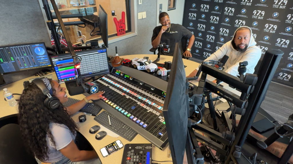 A group of people working in a recording studio, with various audio equipment, computers, and a BMW logo visible.